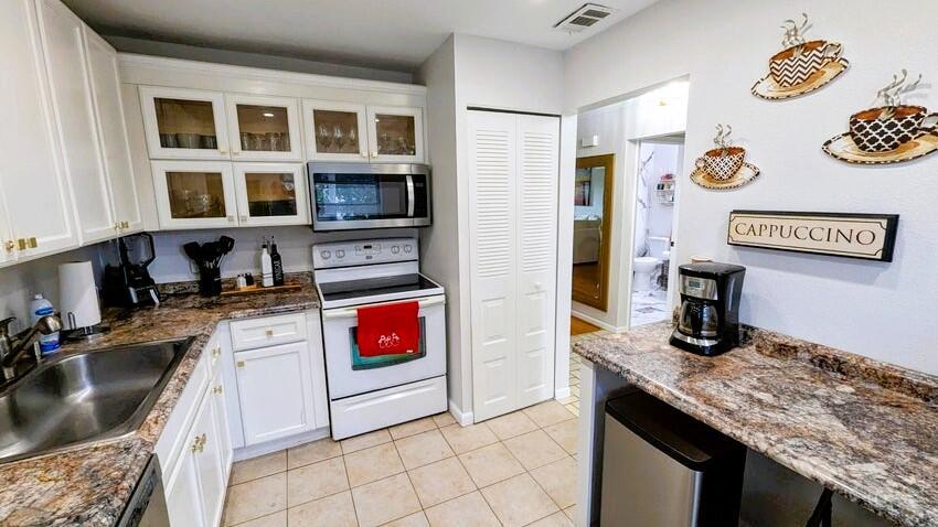 A kitchen features white cabinetry, granite countertops, a white stove, and wall-mounted coffee cup decor — 21362 Juego Circle # 33f, Boca Raton FL 33433, BOCA RATON, FL