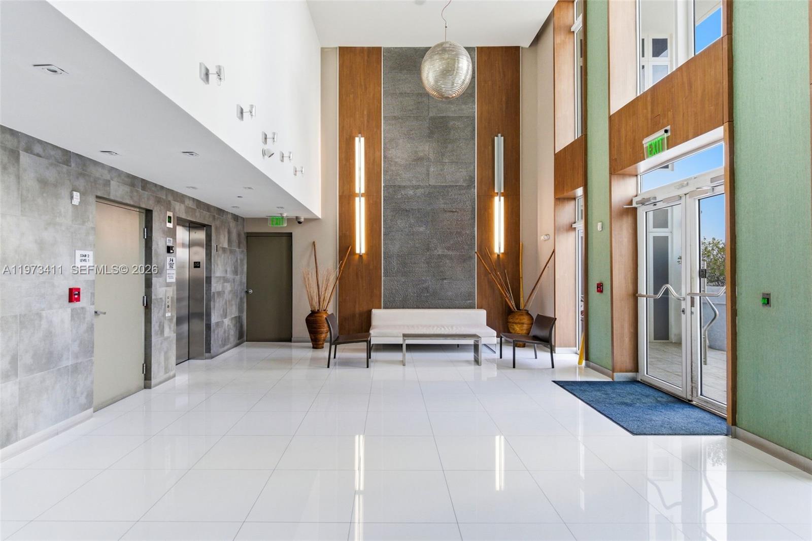 A modern building lobby features white tile floors, a stone accent wall, and glass doors — 448 Ocean Dr # 303, Miami Beach FL 33139, MIAMI BEACH, FL
