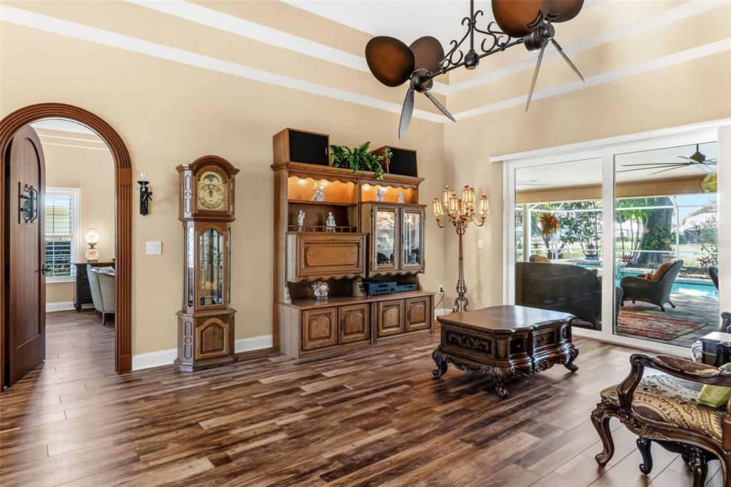 A living room with wood-look flooring, ornate furniture, a unique ceiling fan, and pool views — 8309 SHADOW PINE WAY, SARASOTA, FL