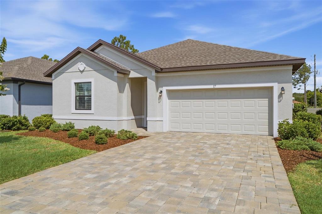 A single-story house with a beige stucco exterior, a two-car garage, and a paver driveway — 17 GREEN CIRCLE, PALM COAST, FL