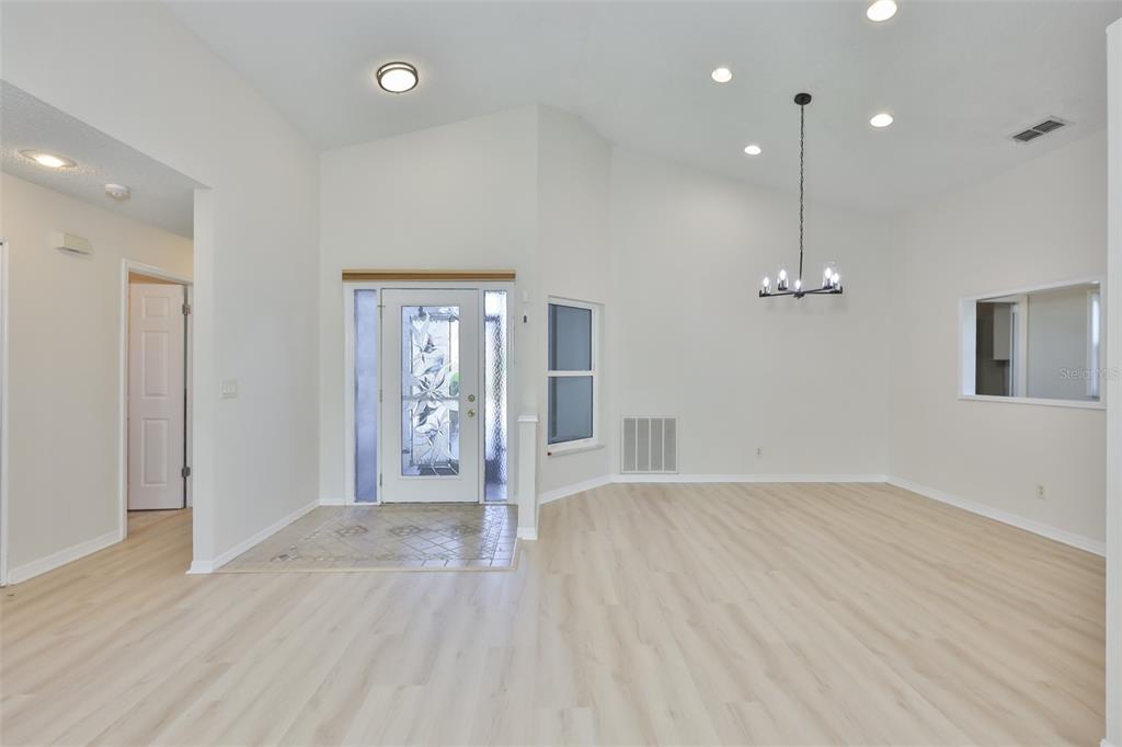 An entryway with light wood flooring, a decorative glass front door, and a dining area — 235 LINGER LANE, SUN CITY CENTER, FL