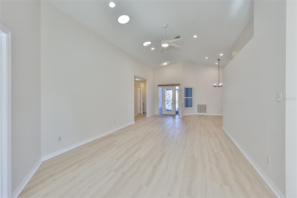 A spacious, empty living room features light wood-look flooring, vaulted ceilings, and recessed lighting — 235 LINGER LANE, SUN CITY CENTER, FL