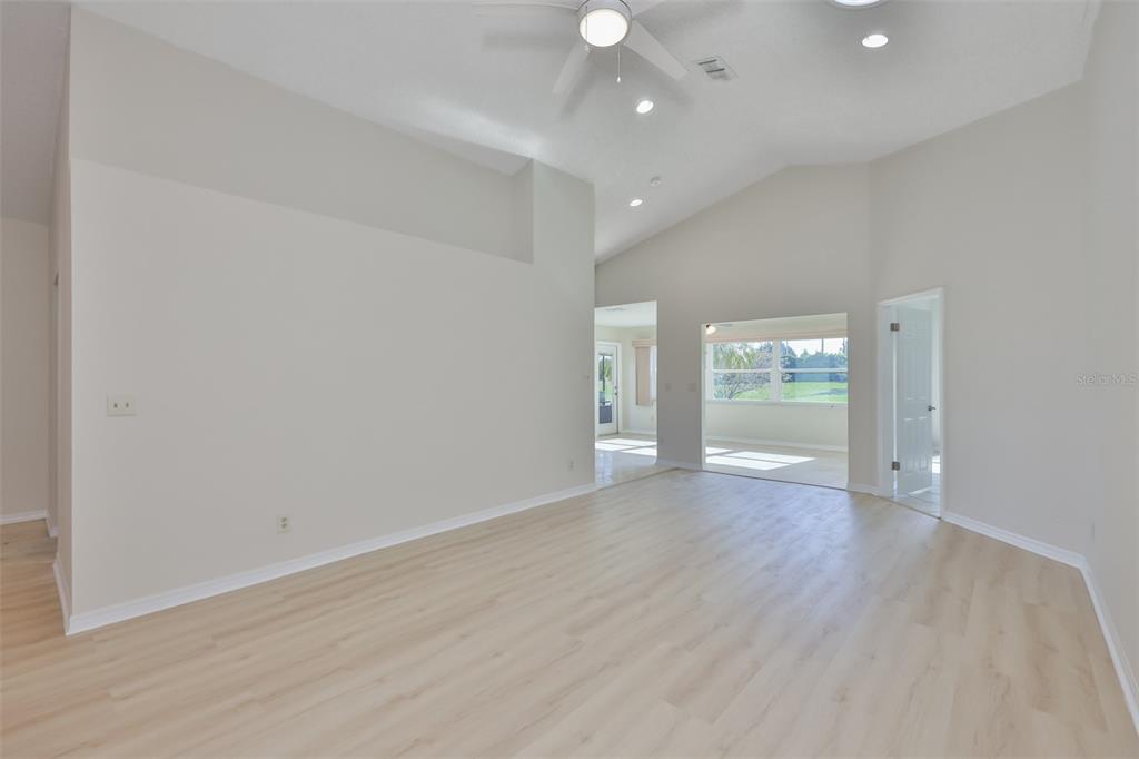 A spacious living room features vaulted ceilings, light wood-look flooring, and a ceiling fan — 235 LINGER LANE, SUN CITY CENTER, FL