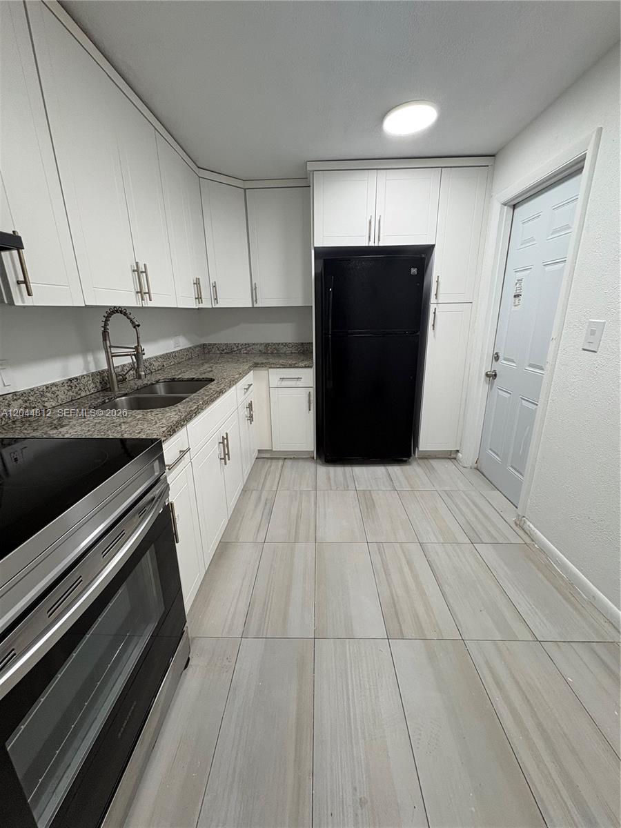 A kitchen features white cabinets, granite countertops, a black refrigerator, and light-colored tile flooring — 447 NE 195th St # 214, Miami FL 33179, MIAMI, FL