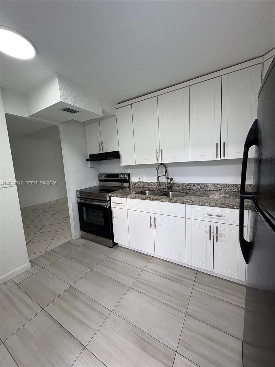 A kitchen features white cabinets, granite countertops, stainless steel appliances, and light-colored tile flooring — 447 NE 195th St # 214, Miami FL 33179, MIAMI, FL