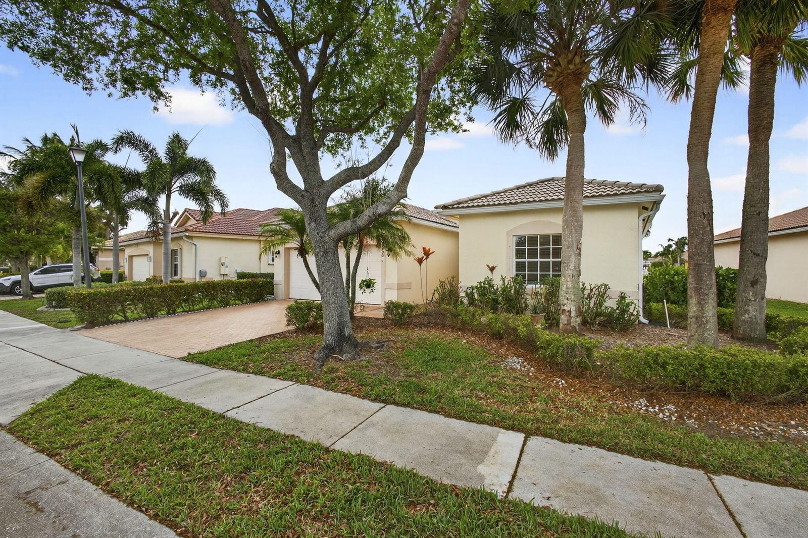 A beige house exterior features a white garage door, brick paver driveway, and front entrance — 8600 Pine Cay, West Palm Beach FL 33411, WEST PALM BEACH, FL