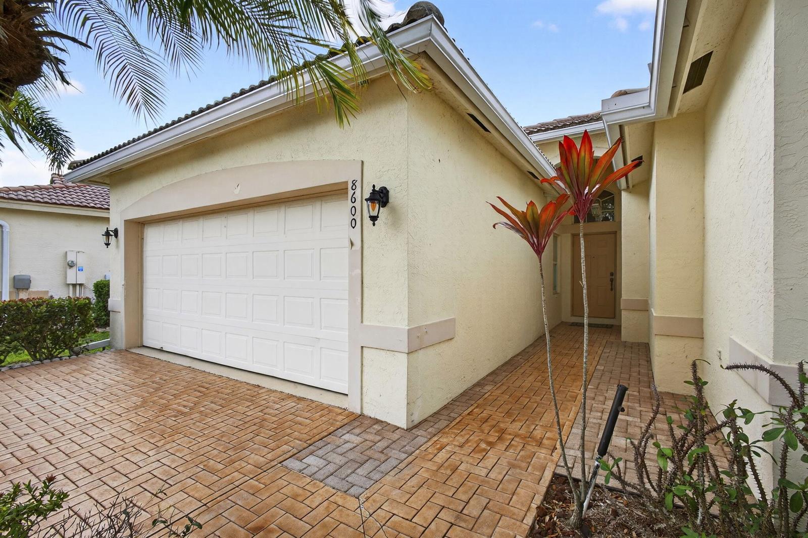 A covered entryway features a tan door, a brick floor, and a window with blinds — 8600 Pine Cay, West Palm Beach FL 33411, WEST PALM BEACH, FL