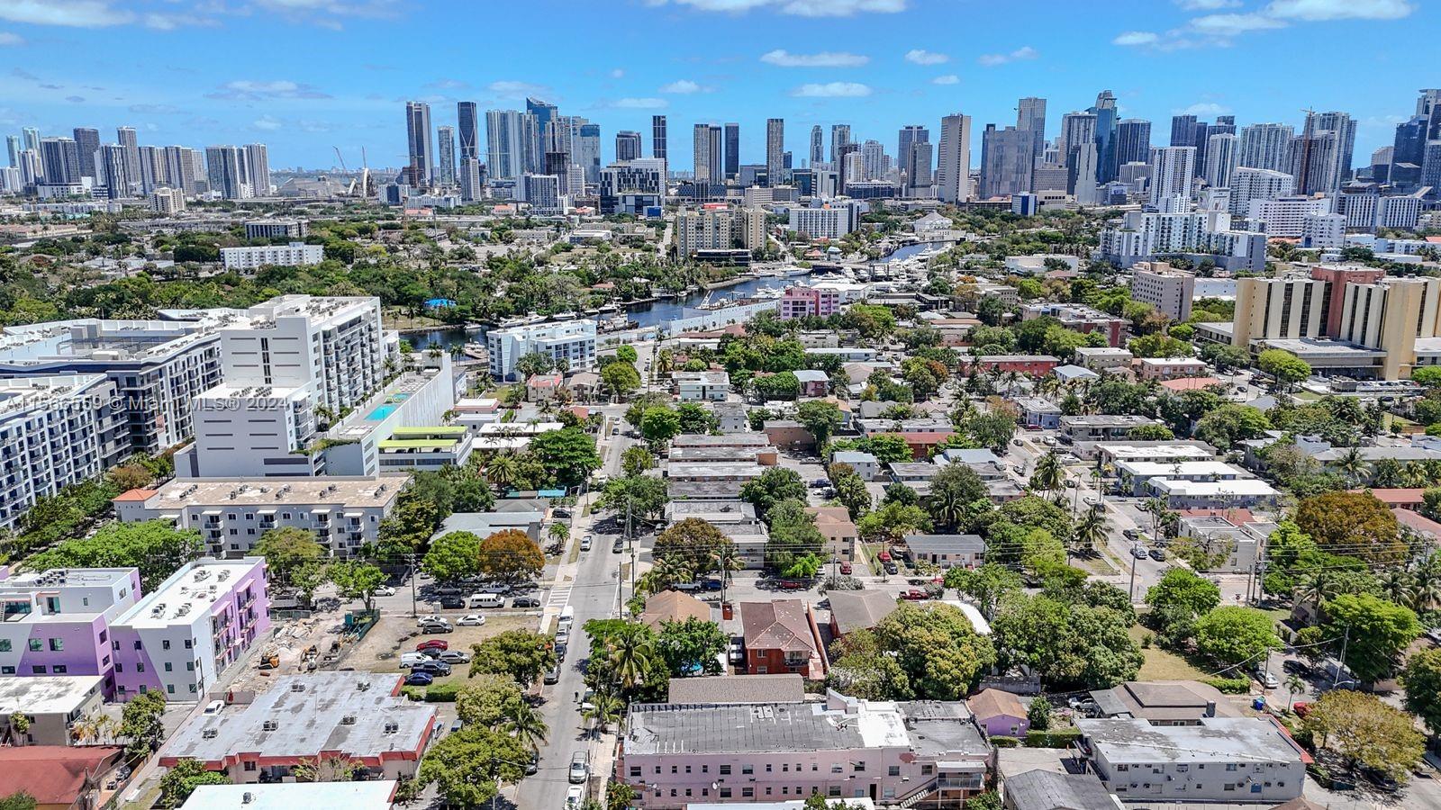An aerial view shows a residential neighborhood with low-rise buildings in the foreground and a city skyline — 1111 NW 6th St, Miami FL 33136, MIAMI, FL