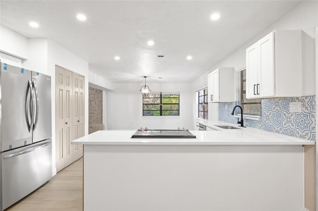 A kitchen features a white island with a cooktop, stainless refrigerator, and patterned blue backsplash — 8057 SHAW ROAD, BROOKSVILLE, FL