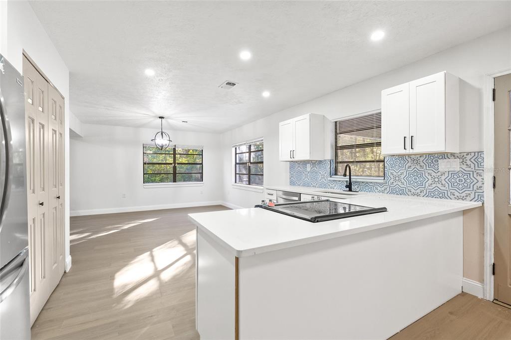 A bright kitchen with white cabinets, a patterned tile backsplash, and an adjacent dining area — 8057 SHAW ROAD, BROOKSVILLE, FL