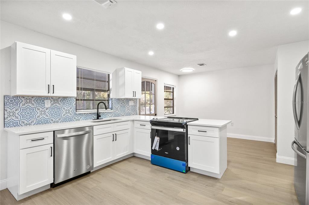 A kitchen with white cabinets, stainless steel appliances, and a blue patterned tile backsplash — 8057 SHAW ROAD, BROOKSVILLE, FL