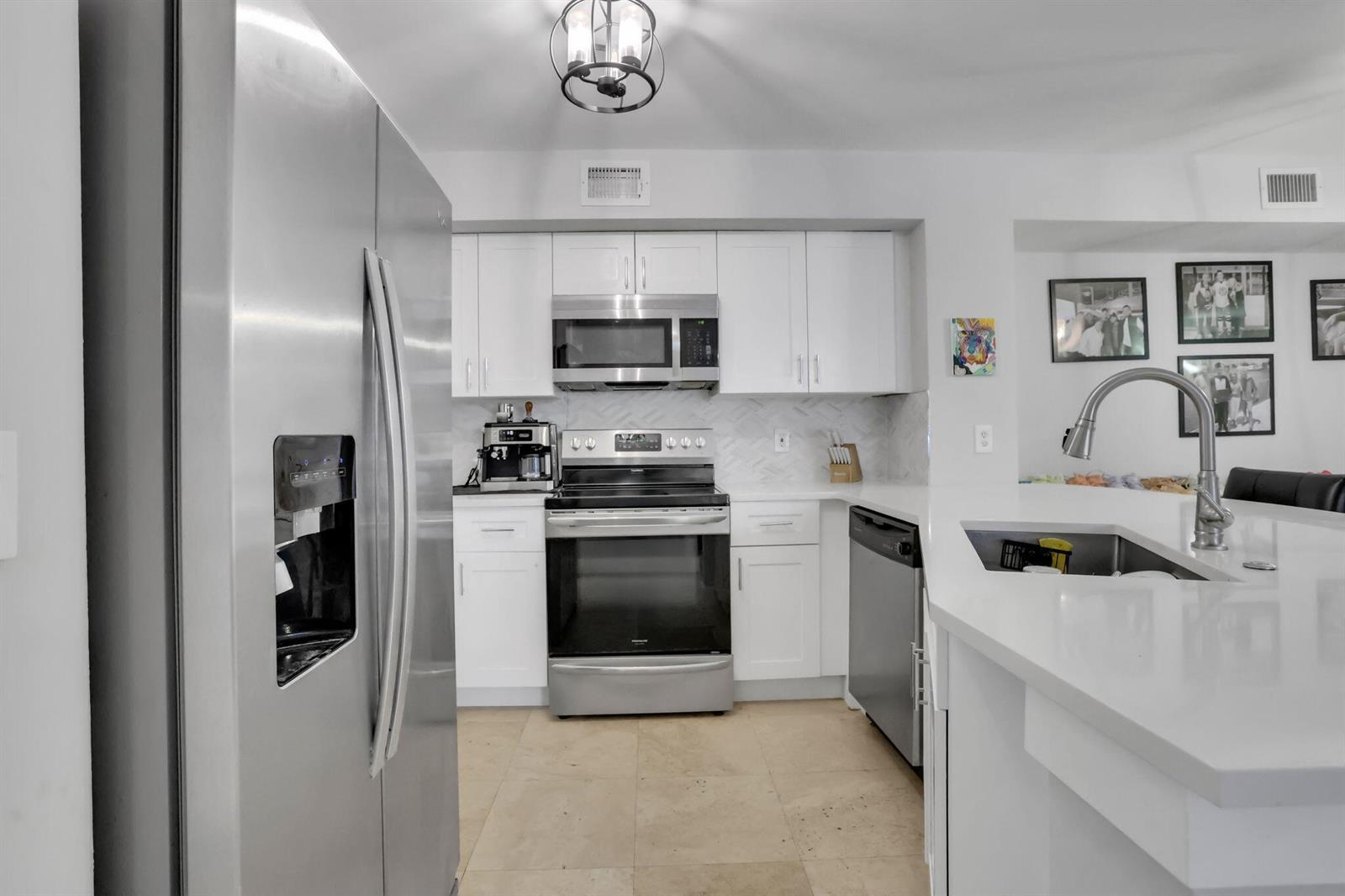 A modern kitchen features white cabinets, stainless steel appliances, and a white quartz island countertop — 3237 Clint Moore Road # 103, Boca Raton FL 33496, BOCA RATON, FL