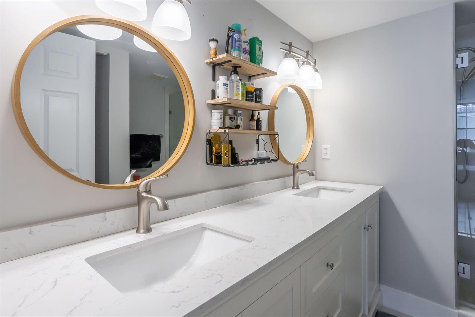 A bathroom vanity features two round wooden mirrors, white marble countertops, and open wall shelving — 3237 Clint Moore Road # 103, Boca Raton FL 33496, BOCA RATON, FL