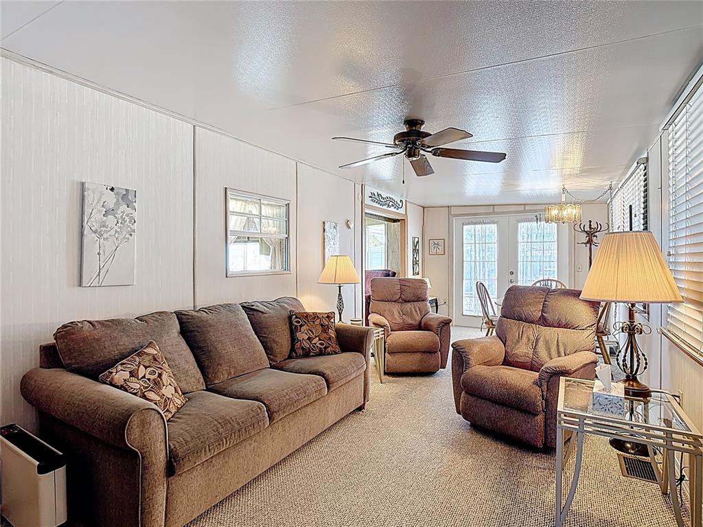 A living room features a brown sofa, two recliners, a ceiling fan, and carpeted flooring — 9000 US HWY 192 UNIT 849, CLERMONT, FL
