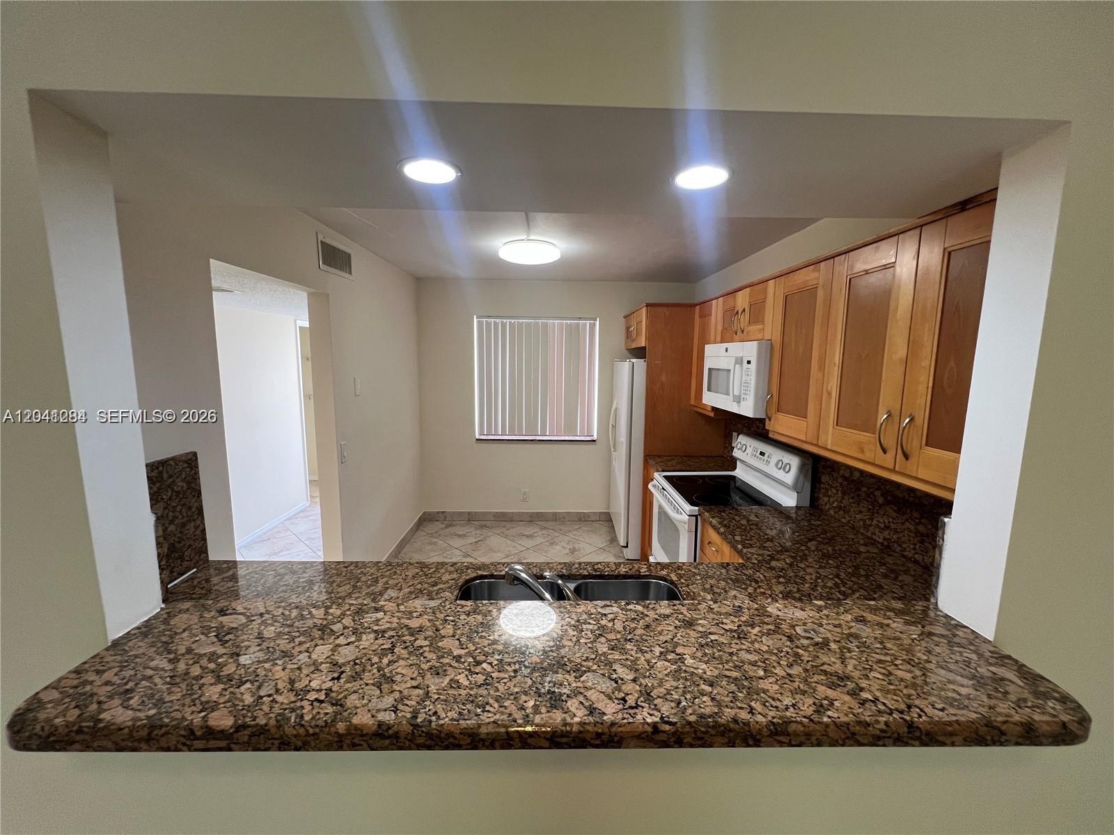 A kitchen features a granite countertop, wooden cabinets, and a pass-through window to a dining area — 379 Lakeview Dr # 205, Weston FL 33326, WESTON, FL