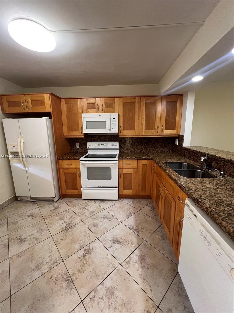 A kitchen features wooden cabinets, white appliances, and granite countertops over tiled flooring — 379 Lakeview Dr # 205, Weston FL 33326, WESTON, FL