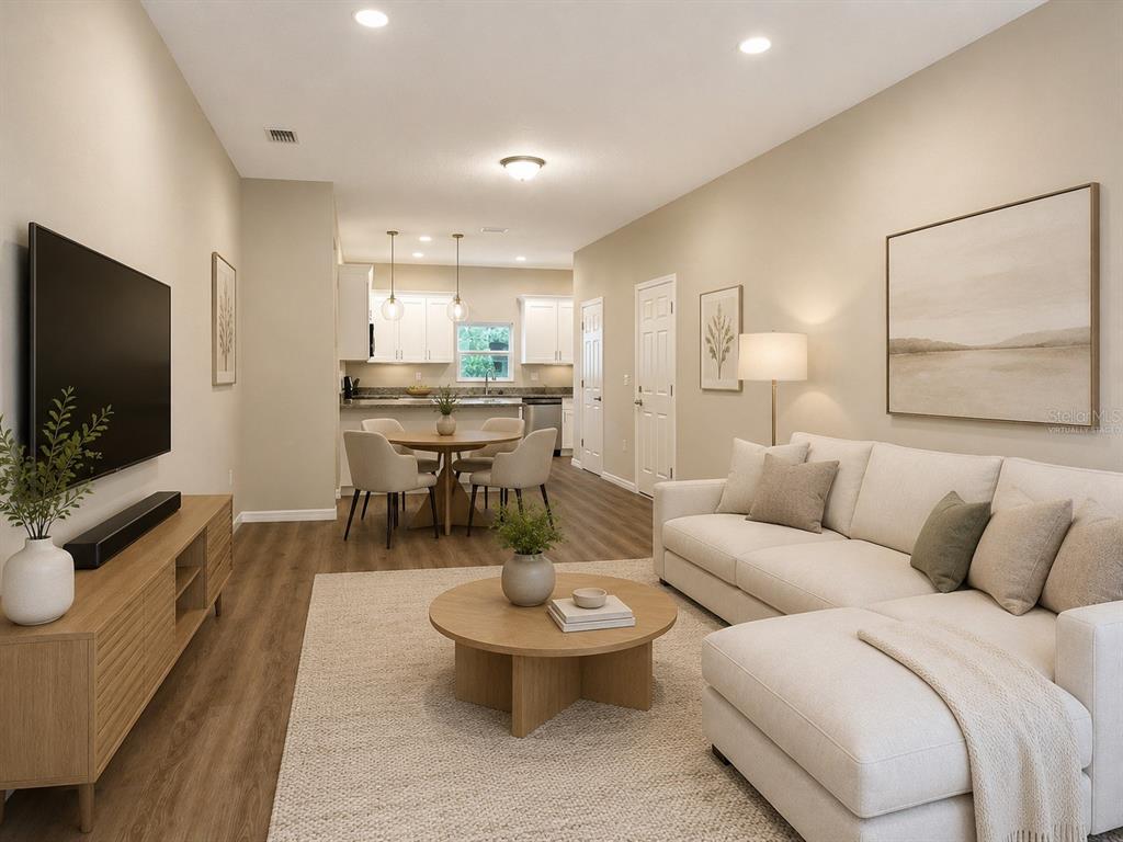 This virtually staged living room features light wood flooring, a sectional sofa, and an open kitchen — 5028 FINDERS COURT, TAMPA, FL