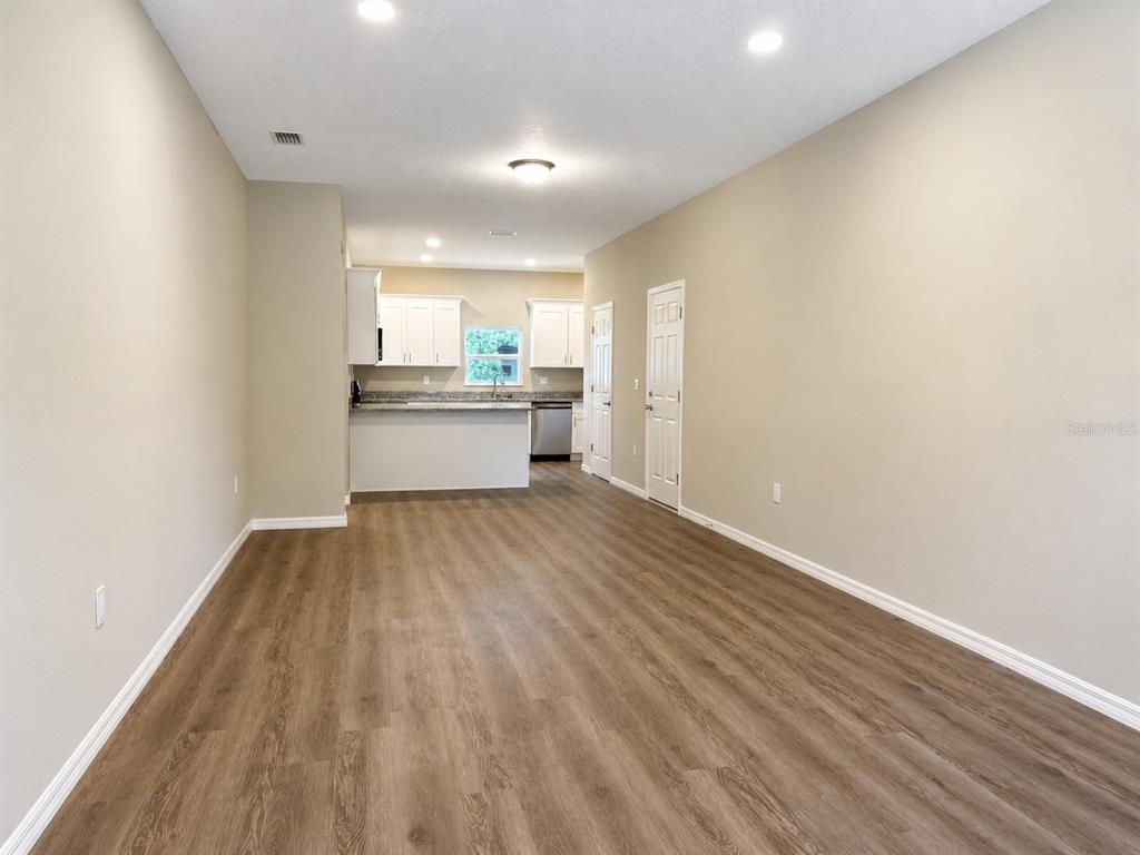 An open-concept living area features light-colored walls, wood-look flooring, and a kitchen in the background — 5028 FINDERS COURT, TAMPA, FL