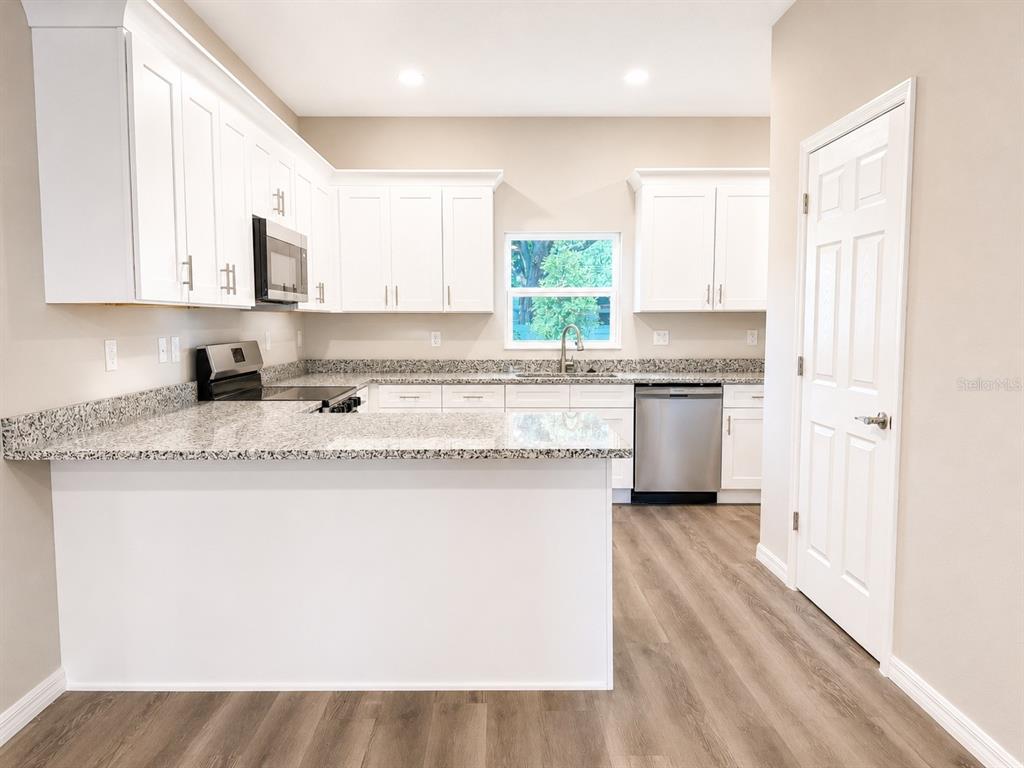 A kitchen features white cabinets, granite countertops, stainless steel appliances, and wood-look flooring — 5028 FINDERS COURT, TAMPA, FL