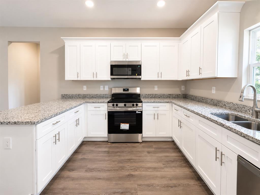 A kitchen with white cabinets, granite countertops, stainless steel appliances, and wood-look flooring — 5028 FINDERS COURT, TAMPA, FL