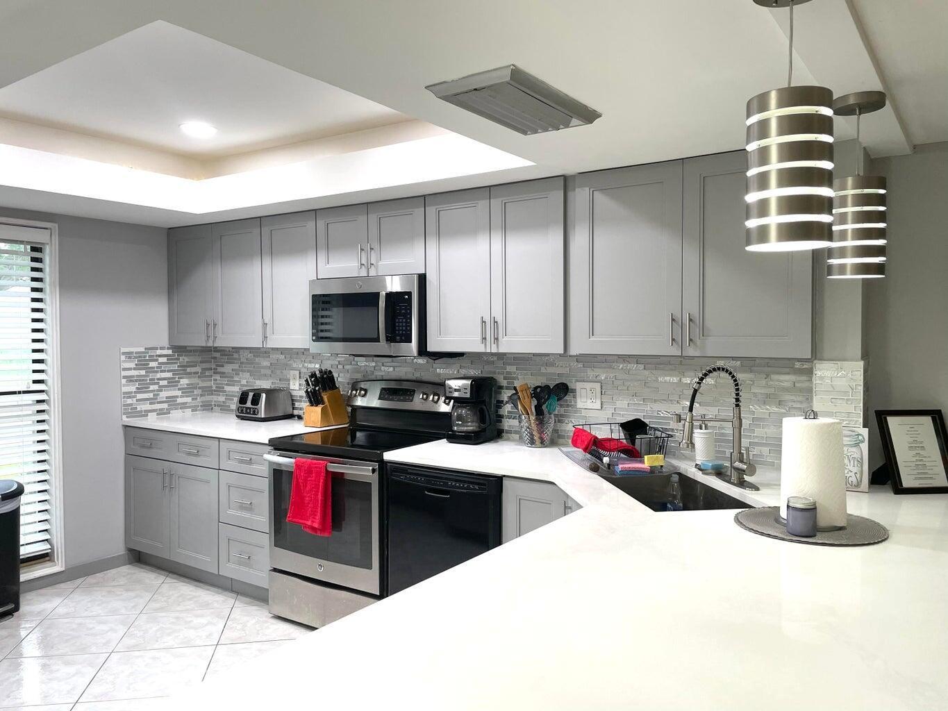A kitchen with grey cabinets, white countertops, a tiled backsplash, and stainless steel appliances — 1714 Consulate Place # 101, West Palm Beach FL 33401, WEST PALM BEACH, FL