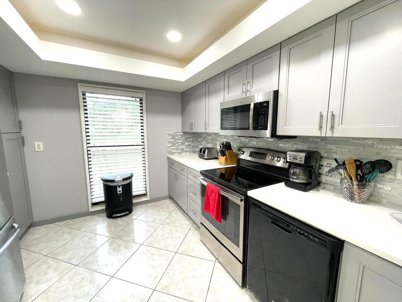 A kitchen features gray cabinets, stainless steel appliances, white countertops, and a tiled backsplash — 1714 Consulate Place # 101, West Palm Beach FL 33401, WEST PALM BEACH, FL