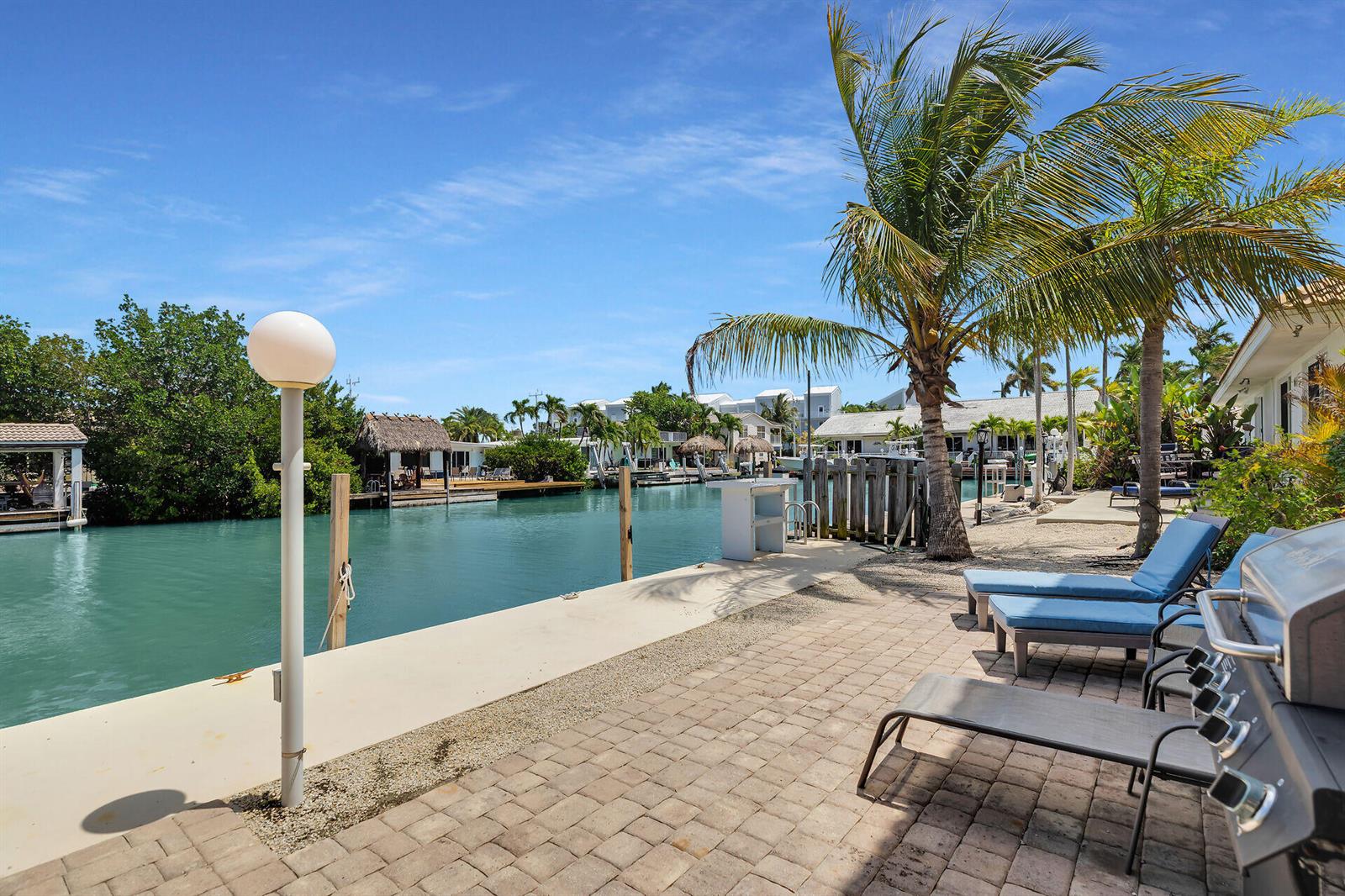 A paved patio with lounge chairs and a grill overlooks a canal with boat docks — 180 9th Street, FL 33051, FL