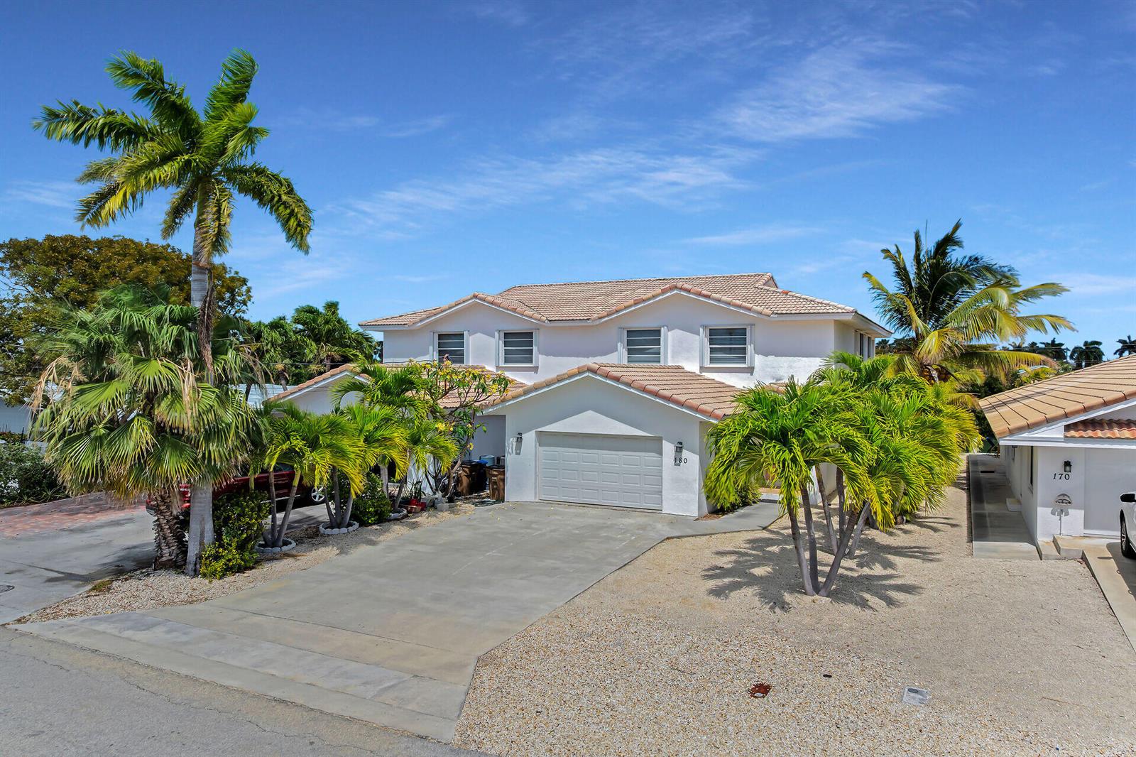 A two-story house with a beige tile roof, a garage, and palm trees in front — 180 9th Street, FL 33051, FL