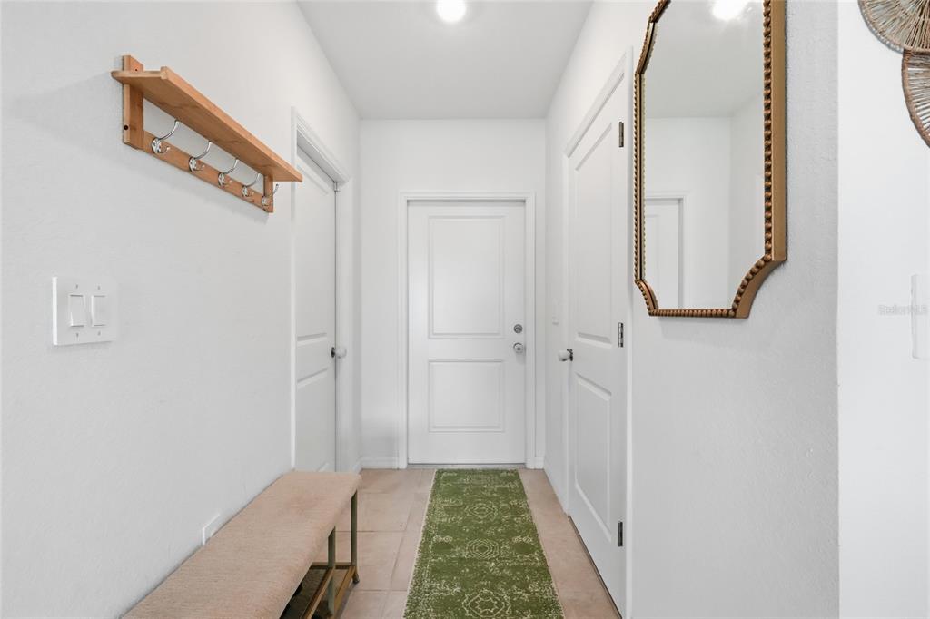 A bright entryway features a wooden coat rack, a bench, a mirror, and a green runner — 14215 LILAC SKY TERRACE, BRADENTON, FL
