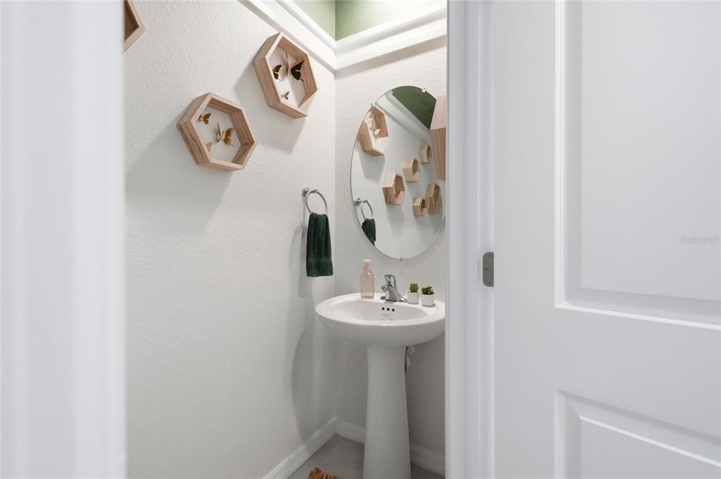 A small powder room features a pedestal sink, an oval mirror, and hexagonal wall shelves — 14215 LILAC SKY TERRACE, BRADENTON, FL