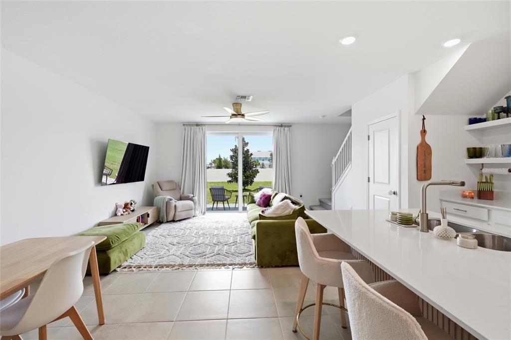 An open-concept living room and kitchen with white walls, tile floors, and a sliding door — 14215 LILAC SKY TERRACE, BRADENTON, FL