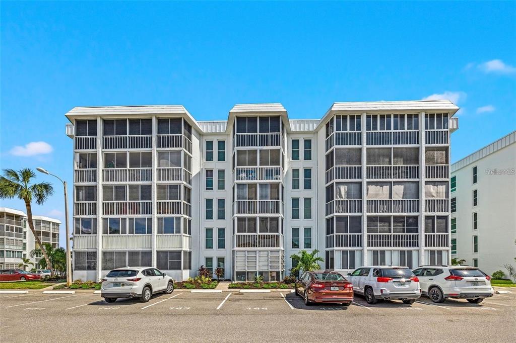 A multi-story white apartment building with screened balconies stands behind a paved parking lot — 4908 38TH WAY S UNIT 501, ST PETERSBURG, FL
