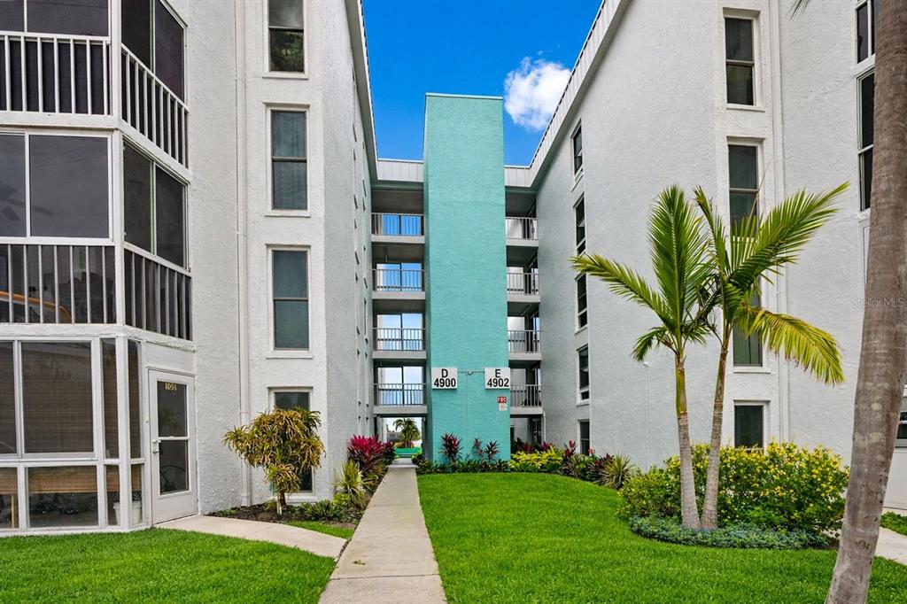 A walkway leads between two white apartment buildings with a central teal stairwell — 4908 38TH WAY S UNIT 501, ST PETERSBURG, FL