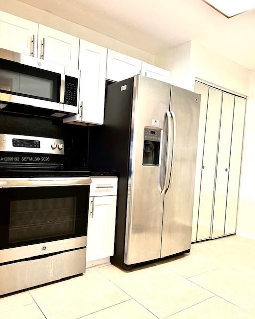 A kitchen features white cabinets, stainless steel appliances, and light-colored tile flooring — 871 NE 207th Ter # 101, Miami FL 33179, MIAMI, FL