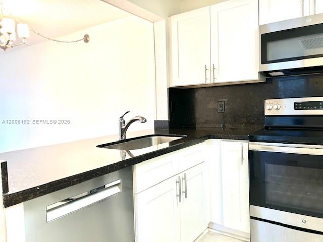 A kitchen features white cabinets, a dark countertop, a stainless steel dishwasher, and a microwave — 871 NE 207th Ter # 101, Miami FL 33179, MIAMI, FL
