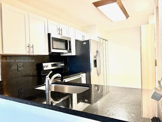 A kitchen features white cabinets, dark countertops, a stainless steel sink, and stainless steel appliances — 871 NE 207th Ter # 101, Miami FL 33179, MIAMI, FL