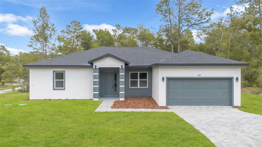 A single-story house with a gray garage, white stucco walls, and a paved driveway — 9651 W PINEVIEW WAY, DUNNELLON, FL