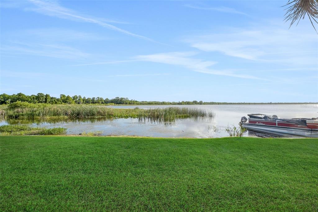 A grassy lawn overlooks a lake with a pontoon boat docked near the shore — 606 ORANGE BLOSSOM DRIVE, WINTER HAVEN, FL