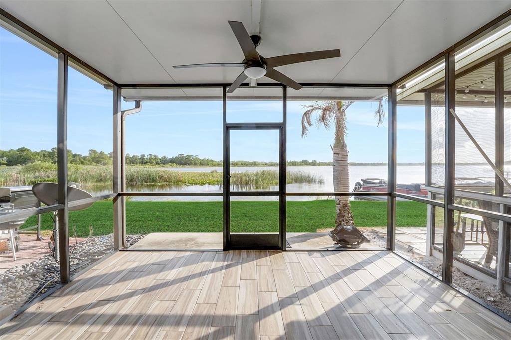 A screened-in porch with wood-look tile flooring overlooks a grassy lawn and a lake — 606 ORANGE BLOSSOM DRIVE, WINTER HAVEN, FL