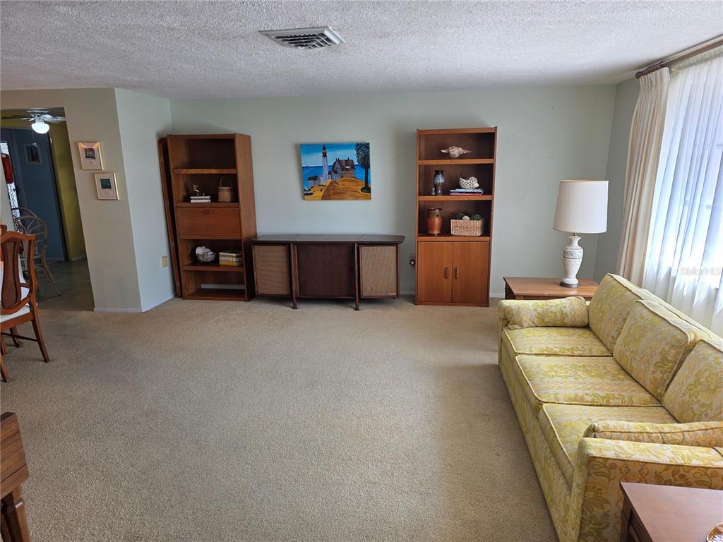 A living room features a patterned sofa, wooden shelving units, and a central console table — 7207 ASHWOOD DRIVE, PORT RICHEY, FL