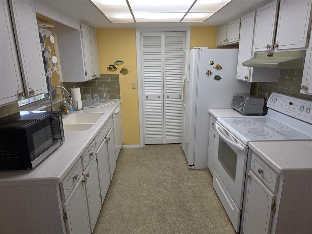 A galley kitchen features white cabinets, yellow walls, a white refrigerator, and a white stove — 7207 ASHWOOD DRIVE, PORT RICHEY, FL