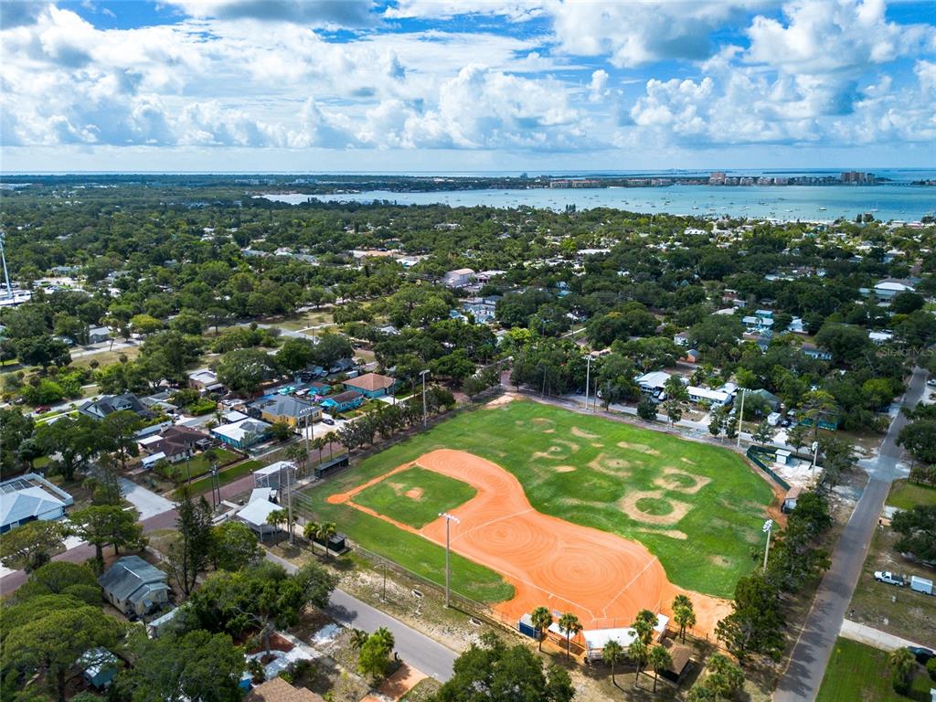 An aerial view shows a baseball field surrounded by residential houses and a distant bay — 1714 55TH STREET S, GULFPORT, FL