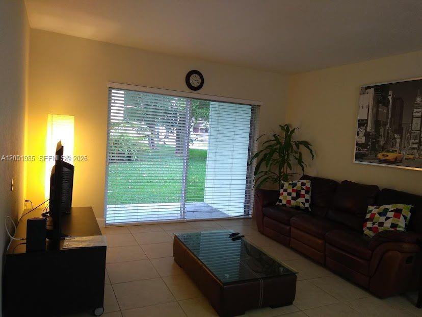 A living room features a dark leather sofa, a glass-topped coffee table, and sliding glass doors — 7530 SW 82nd St # G102, Miami FL 33143, MIAMI, FL