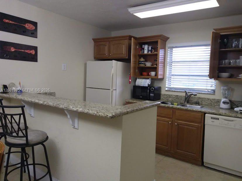 A kitchen features wood cabinets, granite countertops, a white refrigerator, and a breakfast bar — 7530 SW 82nd St # G102, Miami FL 33143, MIAMI, FL
