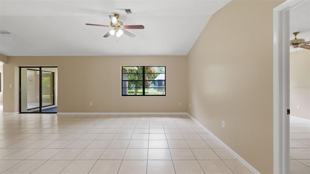An empty room with beige walls, tile flooring, a ceiling fan, and a large window — 8296 GALLUP ROAD, SPRING HILL, FL