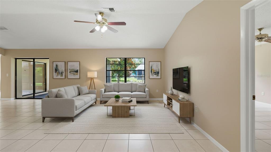 A living room features light tile floors, a ceiling fan, and a neutral-toned furniture arrangement — 8296 GALLUP ROAD, SPRING HILL, FL
