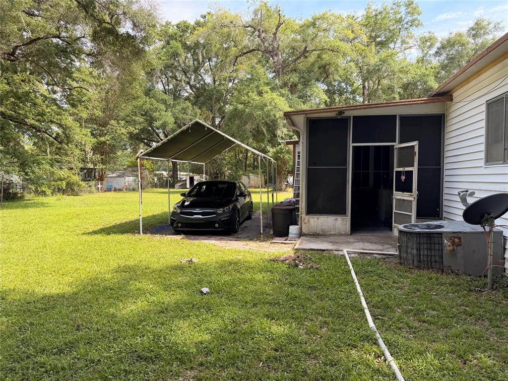 A black car is parked under a metal carport next to a screened-in porch — 201 NW 136TH TERRACE, OCALA, FL