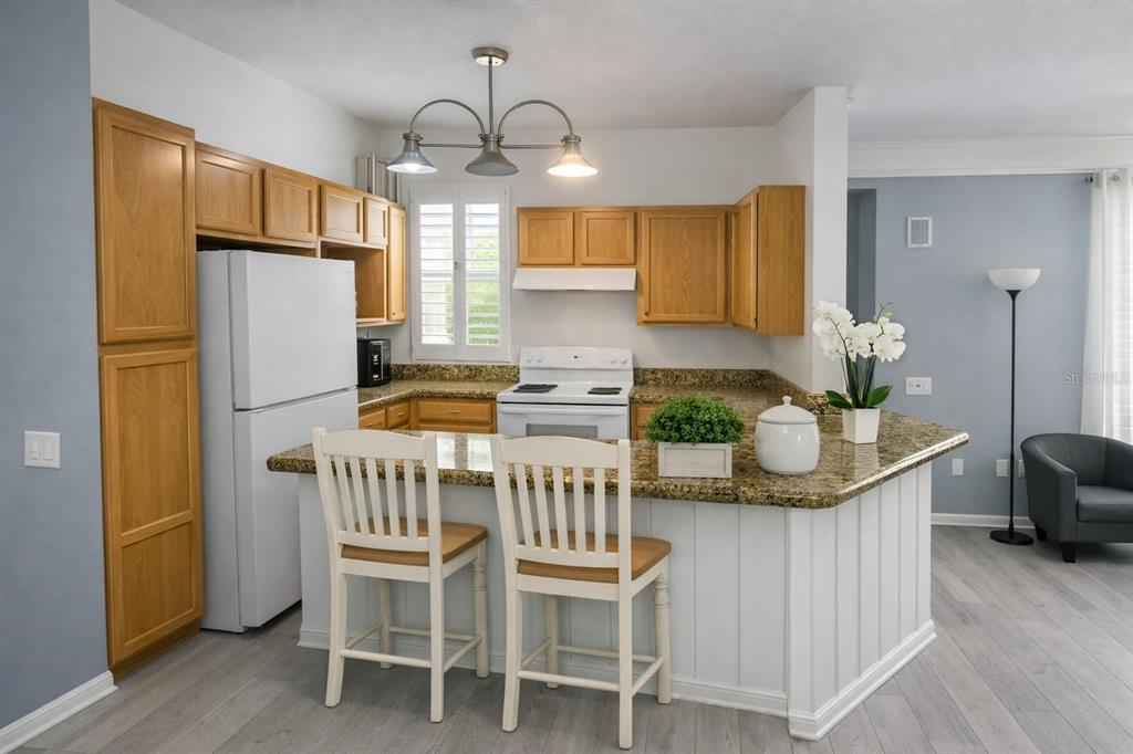 A kitchen features wood cabinets, granite countertops, a white island with seating, and light flooring — 3016 BONFIRE BEACH DRIVE UNIT 104, KISSIMMEE, FL