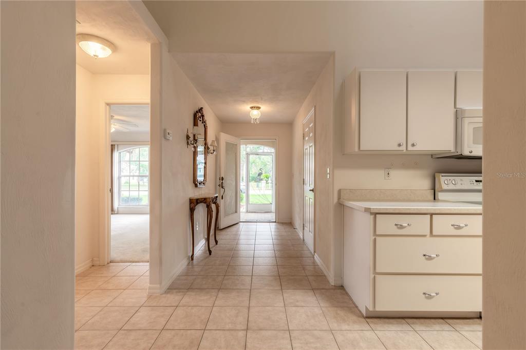 A tiled hallway leads from a kitchen toward an open front door and a living area — 2626 TURNBULL ESTATES DRIVE, NEW SMYRNA BEACH, FL