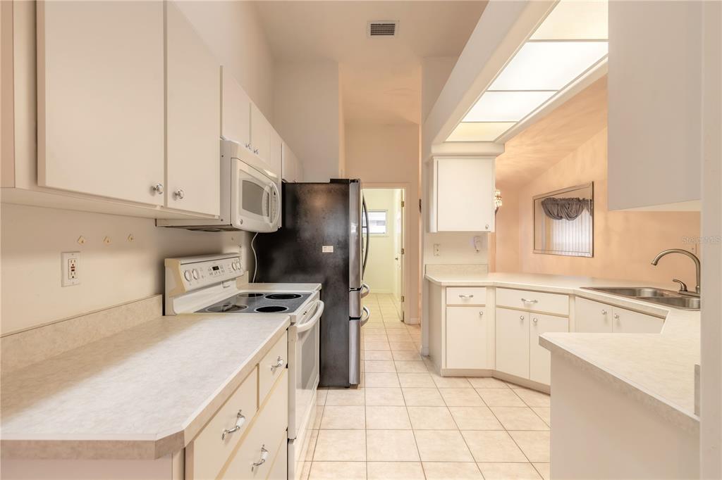 A kitchen features white cabinets, laminate countertops, a black refrigerator, and light-colored tile flooring — 2626 TURNBULL ESTATES DRIVE, NEW SMYRNA BEACH, FL